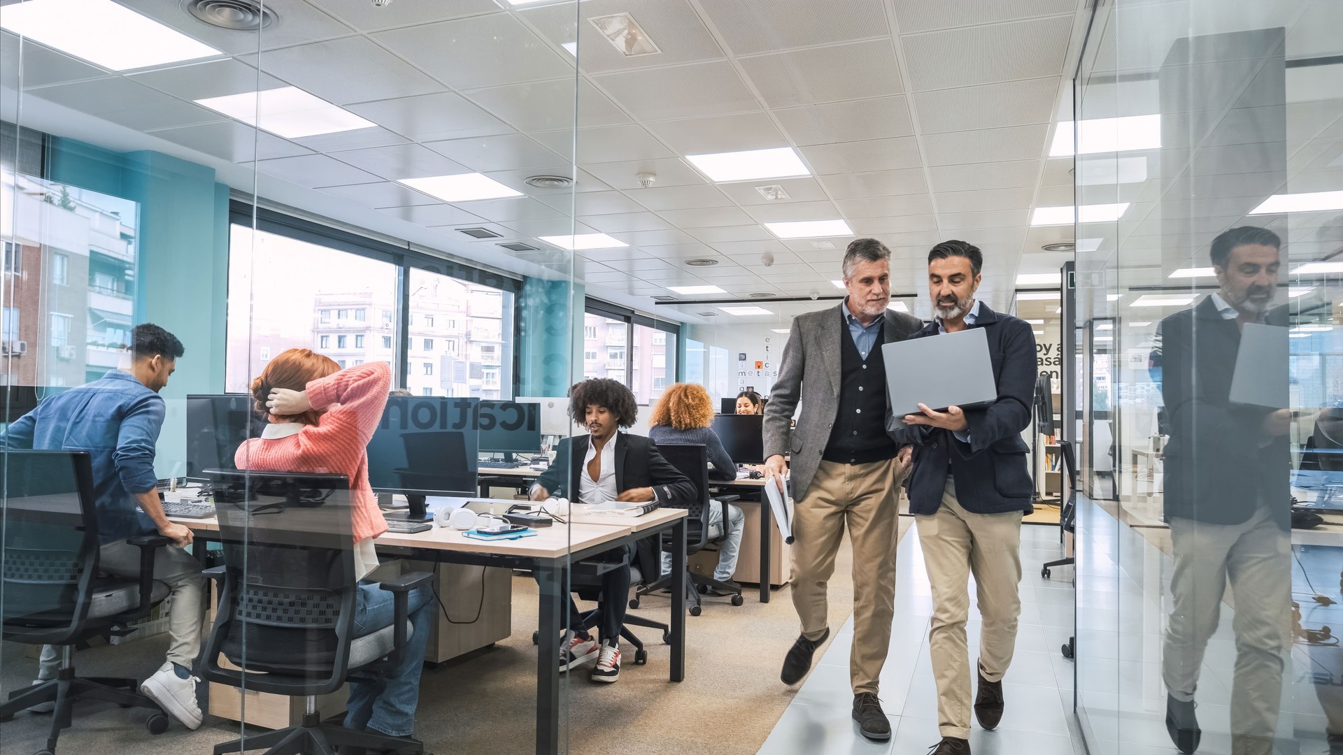 Managers using laptop while walking along computer desks in office